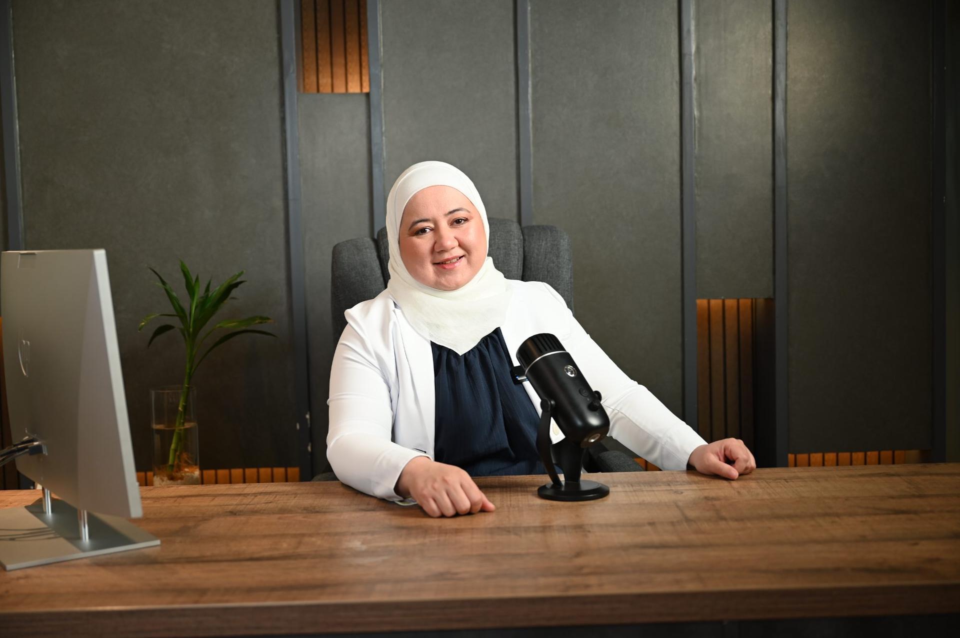 د. دانا أبوروائح إلى مكتبها أمام حاسوب محمول وميكروفون