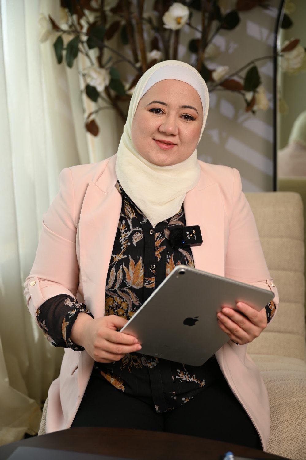 د. دانا أبوروائح جالسة تحمل جهازًا لوحيًا
